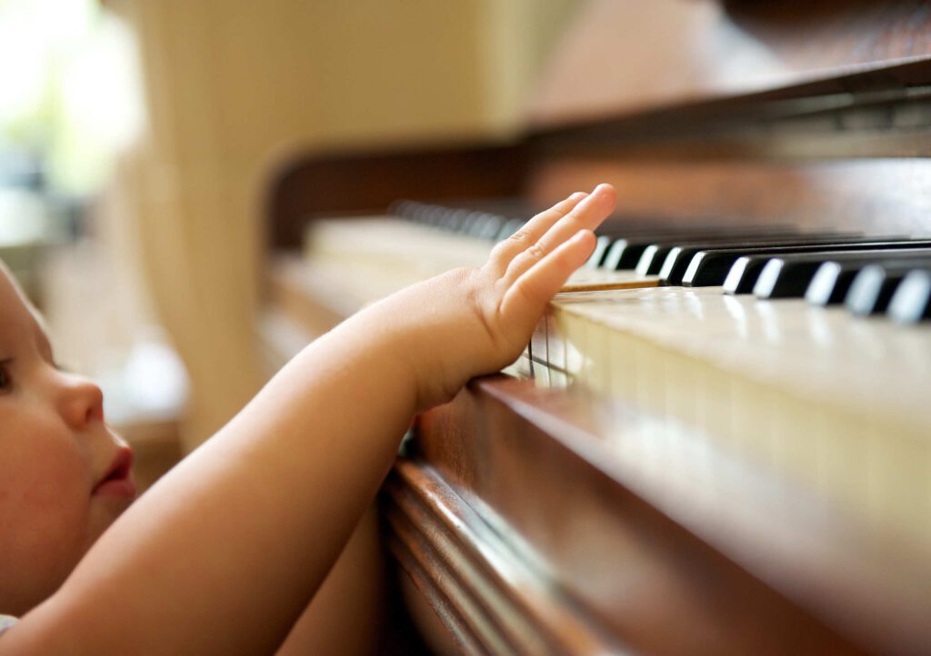 Child reaching up with one hand to tap piano keys; infants program